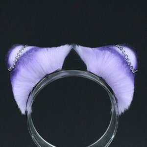 May include: Purple and white faux fur cat ears headband with silver chains. The headband is made of clear plastic.