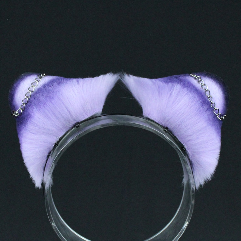 May include: Purple and white faux fur cat ears headband with silver chains. The headband is made of clear plastic.