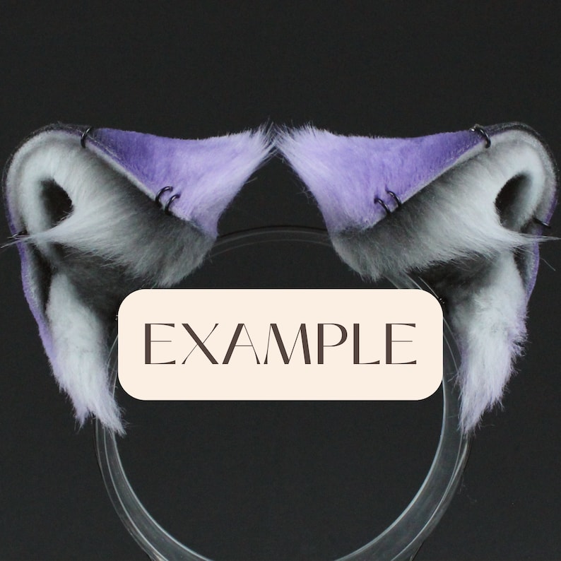 May include: A pair of purple and gray faux fur cat ears with black metal hoops. The ears are attached to a clear plastic headband. The headband is labeled "EXAMPLE".