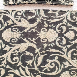 May include: Close-up of a dark grey fabric with an intricate, cream-coloured floral and bird pattern. The design features stylised birds, flowers, and swirling vines, creating a detailed and ornate textile.