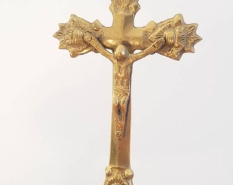 May include: A gold-toned brass crucifix with a candle holder. The crucifix features a detailed figure of Jesus Christ and ornate floral designs.