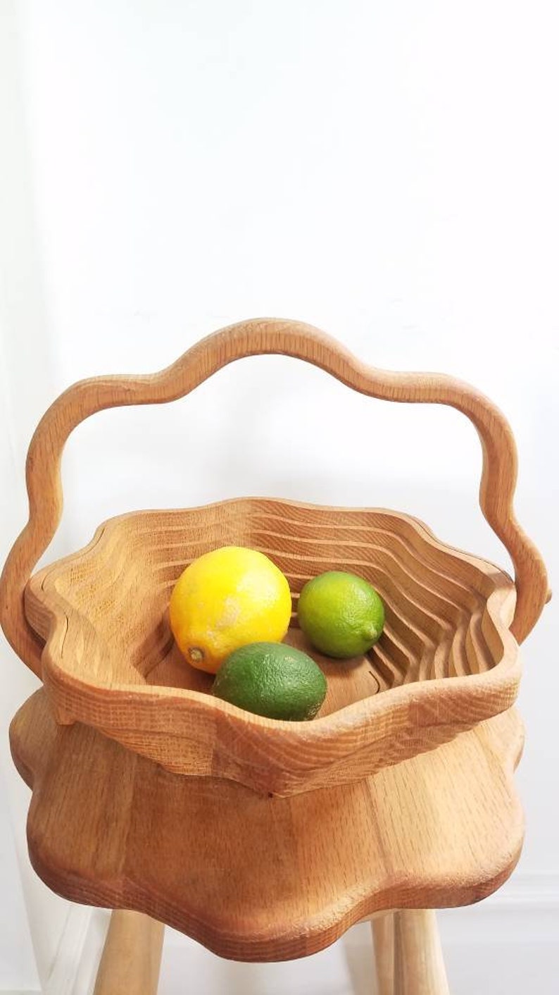 K&ouml;nnte beinhalten: Eine Holzobstschale mit einem einzigartigen, wellenf&ouml;rmigen Design und einem Griff. Die Schale ist mit Zitronen und Limetten gef&uuml;llt.