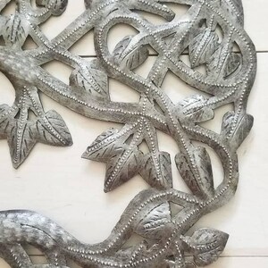 Może przedstawiać: Srebrna metalowa ozdoba ścienna w kształcie drzewa z misternymi wycięciami i wypukłymi kropkami. Drzewo ma liściasty wz&oacute;r z rustykalnym wykończeniem.