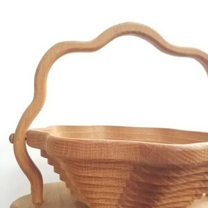 K&ouml;nnte beinhalten: Eine Holzsch&uuml;ssel mit einem einzigartigen, geschichteten Design und einem geschwungenen Griff. Die Sch&uuml;ssel steht auf einem Holzhocker.