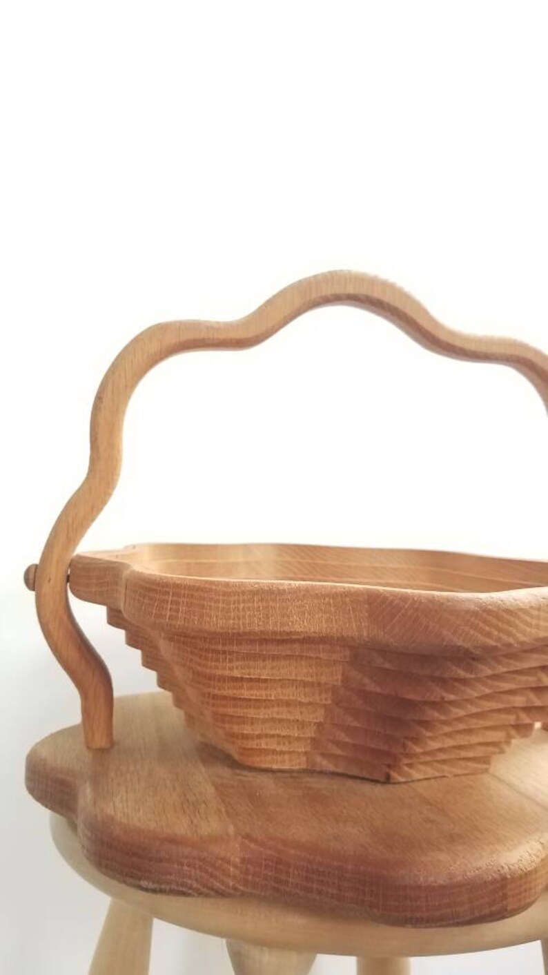 K&ouml;nnte beinhalten: Eine Holzsch&uuml;ssel mit einem einzigartigen, geschichteten Design und einem geschwungenen Griff. Die Sch&uuml;ssel steht auf einem Holzhocker.