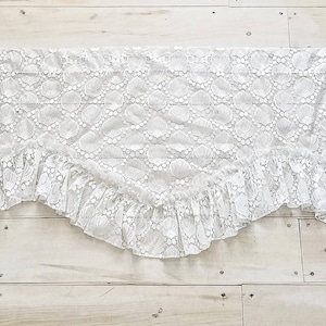 May include: White lace valance with a scalloped edge. The lace has a delicate floral pattern.