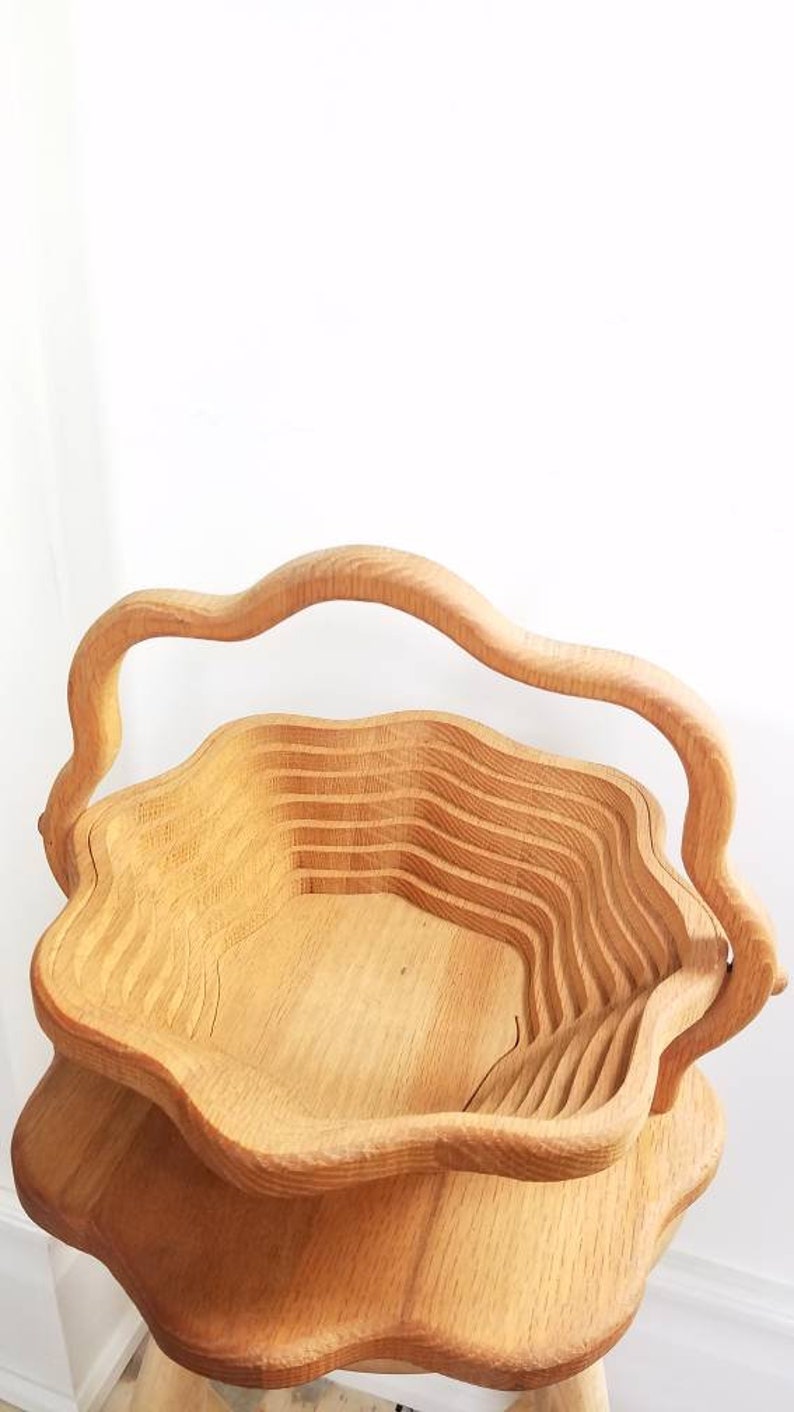 K&ouml;nnte beinhalten: Eine ausziehbare, blumenf&ouml;rmige Servierschale aus Holz mit einem Griff. Die Schale ist aus hellbraunem Holz gefertigt und hat eine nat&uuml;rliche Oberfl&auml;che.