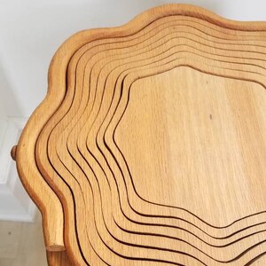 K&ouml;nnte beinhalten: Ein Holztisch mit einem einzigartigen, wellenf&ouml;rmigen Design. Der Tisch besteht aus mehreren Holzschichten, die einen geschichteten Effekt erzeugen. Der Tisch ist hellbraun und hat eine nat&uuml;rliche Holzoptik.