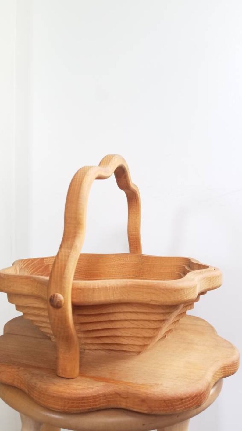 K&ouml;nnte beinhalten: Ein Holzkorb mit einem einzigartigen, gebogenen Griff. Der Korb ist aus hellem braunem Holz gefertigt und hat einen gewellten Rand. Er steht auf einem Holztisch.