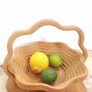 K&ouml;nnte beinhalten: Eine Holzobstschale mit einem einzigartigen, wellenf&ouml;rmigen Design und einem Griff. Die Schale ist mit Zitronen und Limetten gef&uuml;llt.