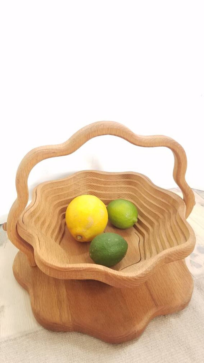 K&ouml;nnte beinhalten: Eine Holzobstschale mit einem einzigartigen, wellenf&ouml;rmigen Design und einem Griff. Die Schale ist mit Zitronen und Limetten gef&uuml;llt.