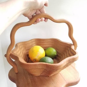 K&ouml;nnte beinhalten: Eine Obstschale aus Holz mit einem einzigartigen, wellenf&ouml;rmigen Design. Die Schale hat einen Griff und ist aus Naturholz gefertigt. Sie ist mit Zitronen und Limetten gef&uuml;llt.