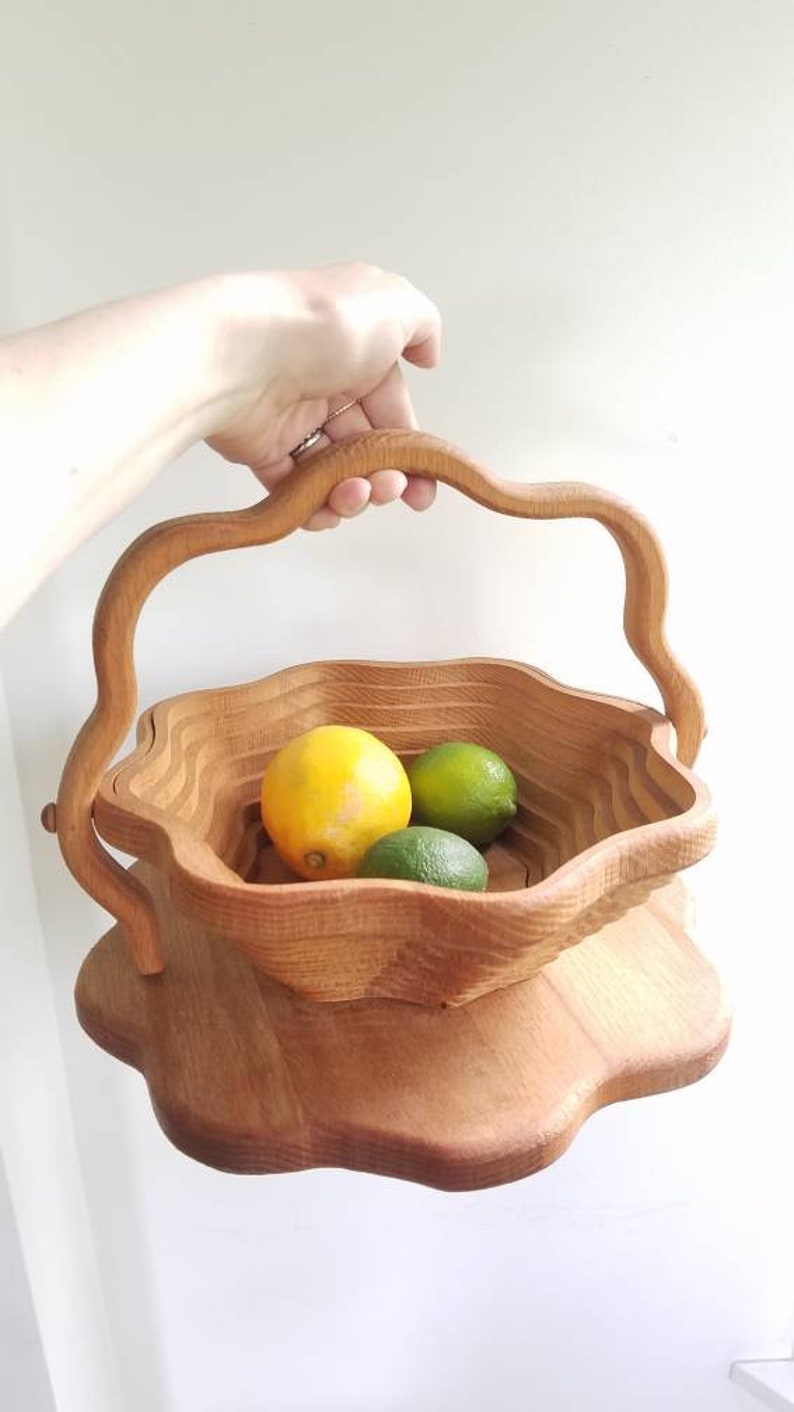 K&ouml;nnte beinhalten: Eine Obstschale aus Holz mit einem einzigartigen, wellenf&ouml;rmigen Design. Die Schale hat einen Griff und ist aus Naturholz gefertigt. Sie ist mit Zitronen und Limetten gef&uuml;llt.