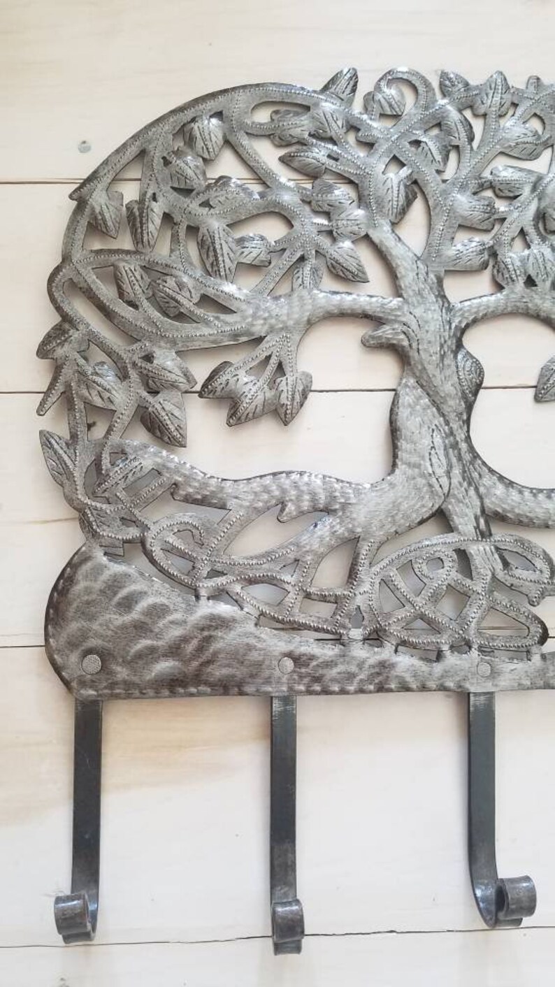 Może przedstawiać: Metalowy wieszak ścienny w kształcie drzewa z trzema haczykami. Drzewo jest srebrne i ma rustykalne wykończenie. Haczyki są wykonane z czarnego metalu.