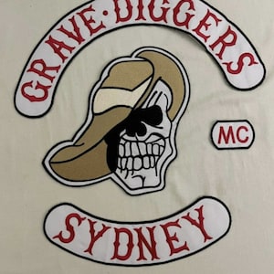 Puede incluir: Parche blanco con texto bordado en rojo "GRAVE DIGGERS MC" y una calavera con un sombrero de vaquero marrón. Debajo hay un parche blanco con texto bordado en rojo "SYDNEY".