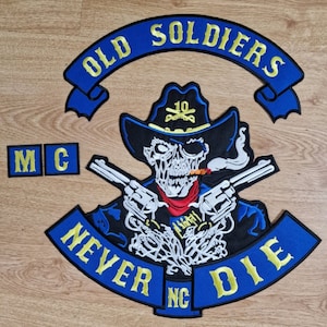 Op de afbeelding: Blauw en geel geborduurd patch met een schedel die een cowboyhoed draagt en twee pistolen vasthoudt. De patch zegt "Old Soldiers Never Die" en "MC" in de linkerbovenhoek.