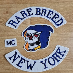 May include: White and blue embroidered patch with the text "RARE BREED MC NEW YORK" and a skull wearing a blue hooded robe.