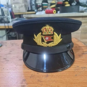 May include: A black wool peaked cap with a gold crown and a red and white flag with a star. The cap has a black leather band with a gold button.