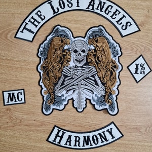 Op de afbeelding: Een set witte en zwarte geborduurde patches met de tekst "The Lost Angels", "Harmony", "MC" en "1%er". De belangrijkste patch toont een skelet met vleugels en een schedel.