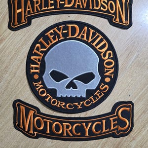 May include: Three Harley-Davidson motorcycle patches. The top patch is a black banner with orange text that reads "Harley-Davidson". The middle patch is a black circle with a silver skull and orange text that reads "Harley-Davidson Motorcycles". The bottom patch is a black banner with orange text that reads "Motorcycles".