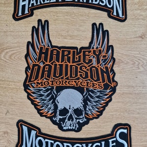 Può includere: Tre toppe per moto Harley-Davidson. La toppa superiore è uno stendardo nero e arancione con il testo "Harley-Davidson". La toppa centrale è una toppa nera e arancione con un teschio e ali, e il testo "Harley-Davidson Motorcycles". La toppa inferiore è uno stendardo nero e arancione con il testo "Motorcycles".