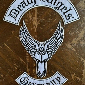 May include: White embroidered patches with black lettering. The top patch reads "Death Angels" in an arched shape. The bottom patch reads "Germany" in an arched shape. A white embroidered patch of an angel with wings spread is in the center.