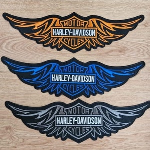 Puede incluir: Tres parches de motocicleta Harley-Davidson con alas bordadas y las palabras "MOTOR", "HARLEY-DAVIDSON" y "CYCLES". Los parches son de color naranja, azul y gris.