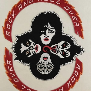 Könnte beinhalten: Ein roter und orangefarbener gestickter Patch mit den Worten "Rock and Roll Over" in einem Kreis. Die Mitte des Patches zeigt vier stilisierte Gesichter der Band KISS in Schwarzweiß.