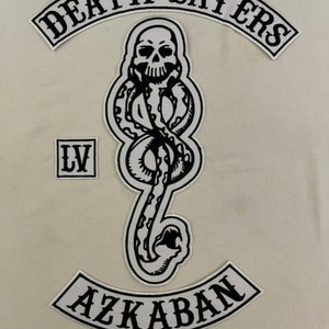 Puede incluir: Parches bordados en blanco y negro con el texto "Death Eaters", "LV" y "Azkaban". El parche del medio presenta una serpiente con una calavera.