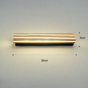 May include: A modern wall light fixture with a wooden frame and integrated LED lights. The light is 50 cm wide and 8 cm high.