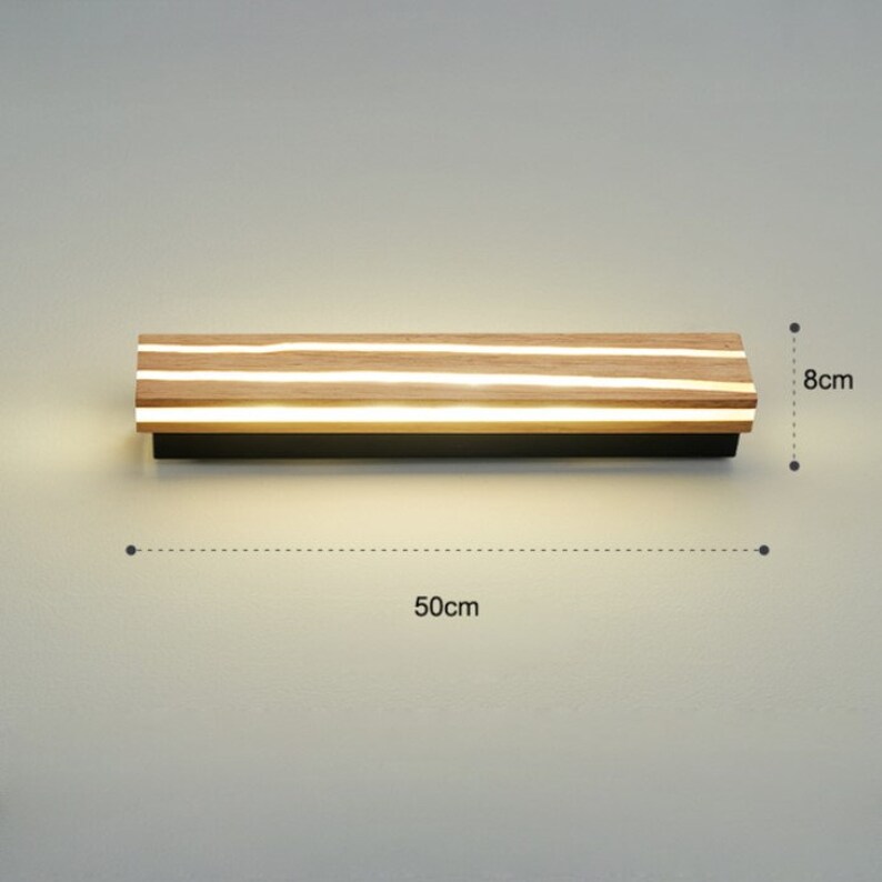 May include: A modern wall light fixture with a wooden frame and integrated LED lights. The light is 50 cm wide and 8 cm high.
