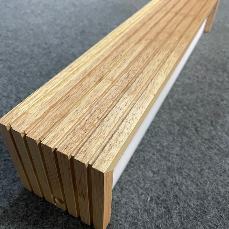 May include: A long, rectangular wooden light fixture with a white diffuser. The fixture is made of multiple thin strips of wood that are stacked on top of each other.