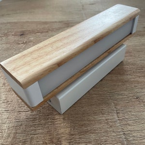 May include: A wooden and white wall light fixture with a rectangular shape. The light fixture has a wooden top and a white base.
