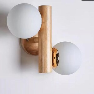 以下が含まれることがあります： 木製の壁掛け照明器具で、白いすりガラスの球体が2つ付いています。照明器具は自然な木の色合いで、シンプルなデザインです。