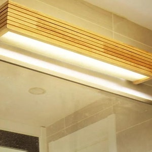 May include: A wooden bathroom vanity light fixture with a rectangular shape and a built-in LED light strip. The light fixture is made of natural wood with a light brown finish.