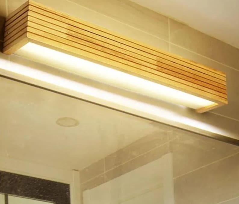 May include: A wooden bathroom vanity light fixture with a rectangular shape and a built-in LED light strip. The light fixture is made of natural wood with a light brown finish.