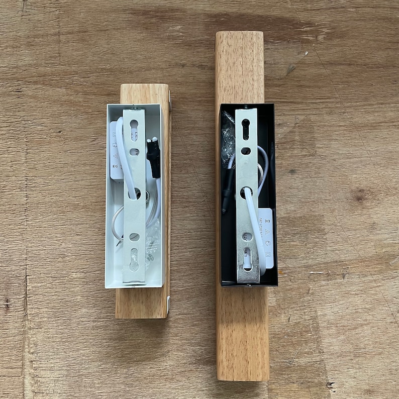 May include: Two wooden wall sconces with white and black electrical wiring and metal mounting plates. The sconces are unfinished and have a natural wood color.