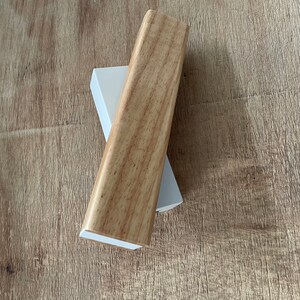 May include: A wooden trim piece with a light brown wood grain finish. The trim piece is sitting on top of a white trim piece.