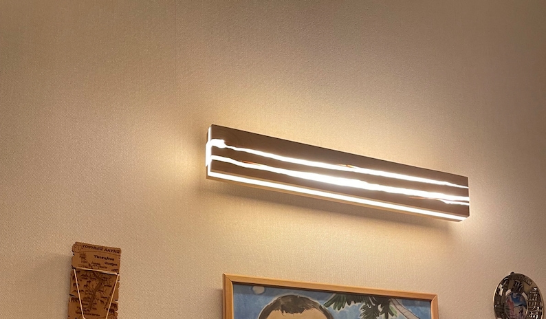 May include: A modern, rectangular, chrome-plated light fixture with two rows of LED lights. The light fixture is mounted on a white wall.