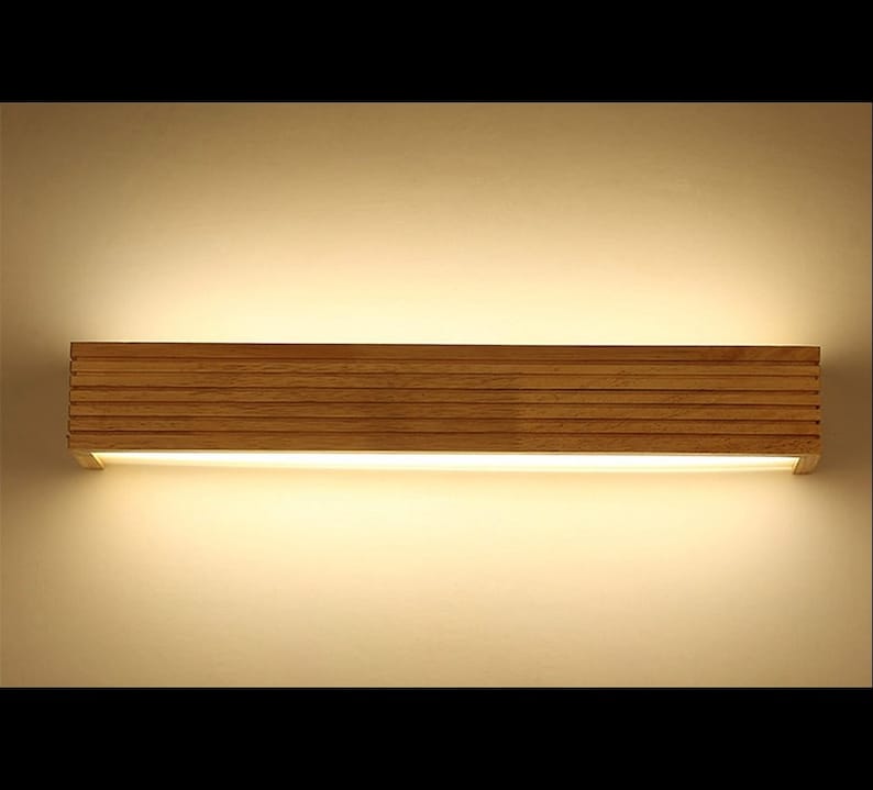 May include: A modern wooden wall light fixture with a rectangular shape and a warm white light. The light is made of natural wood with a slatted design.