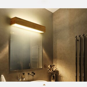 May include: A wooden bathroom vanity light fixture with a rectangular shape and a frosted glass diffuser. The light is mounted above a mirror and a white sink.