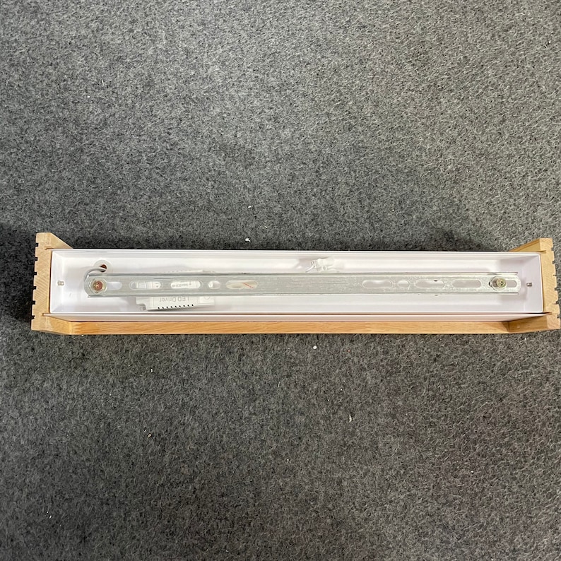 May include: A white light fixture with a wooden frame. The light fixture has a metal track with the text "LED DRIVER" printed on it.