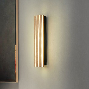 May include: A modern wall sconce with a rectangular wooden frame and a black metal backing. The light fixture has a warm white glow and is illuminated by LED lights.