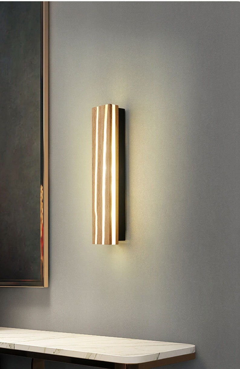 May include: A modern wall sconce with a rectangular wooden frame and a black metal backing. The light fixture has a warm white glow and is illuminated by LED lights.