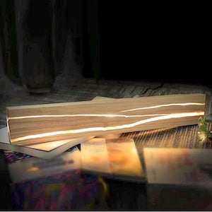 May include: A wooden lamp with a clear resin inlay that illuminates with warm white light. The lamp is resting on a stack of books.