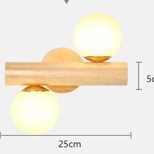 以下が含まれることがあります： 木製の壁掛け照明器具で、すりガラス製の球体が2つ付いています。照明器具の幅は25cm、高さは5cmです。