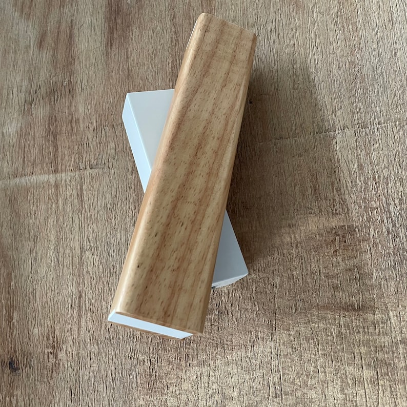 May include: A wooden trim piece with a light brown wood grain finish. The trim piece is sitting on top of a white trim piece.