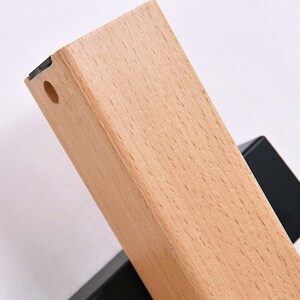 May include: Close-up of a light wood shelf bracket with a black metal base. The bracket has a round hole in the top.