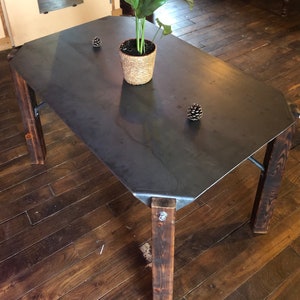 May include: A dark grey metal table top with a rustic wood base. The table is sitting on a hardwood floor and has a small potted plant and two pine cones on the table top.