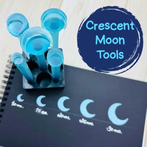 May include: A set of translucent blue crescent moon tools, displayed with a black holder and a notebook. The notebook features crescent moon shapes in various sizes, ranging from 10 mm to 30 mm. The text "Crescent Moon Tools" is in a blue circle.